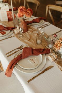 the table is set with white plates and silverware, orange napkins, and flowers