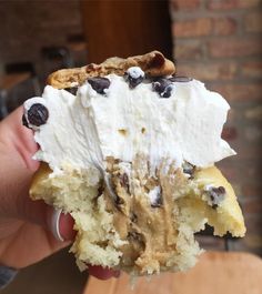 someone holding up a piece of cake with white frosting and chocolate chips on top