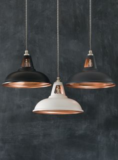 three black and copper pendant lights hanging on a chalkboard wall in an industrial setting