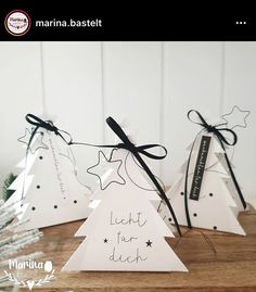 three white christmas trees with black bows on them and one has a message written on it