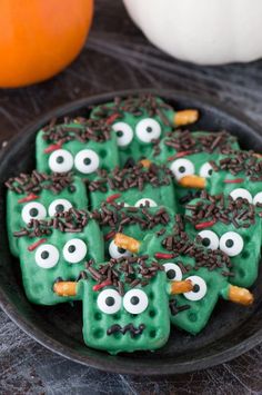 some green cookies with googly eyes and chocolate sprinkles on them in a black plate