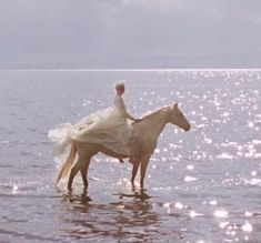 a woman riding on the back of a brown horse in shallow water near shore line