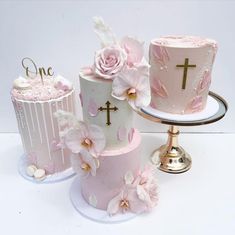 three cakes decorated with pink and white frosting, one has a cross on the top