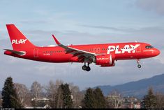 a red plane with play written on it is flying in the sky above some trees