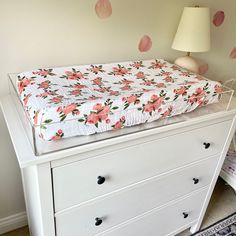 a baby crib with pink flowers on it in a white room next to a lamp