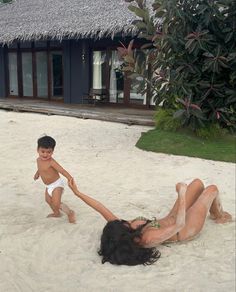 two children playing in the sand on a beach with a hut and pool behind them