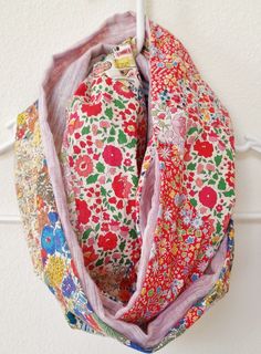 a multicolored scarf hanging from a hook on a white wall with flowers and leaves