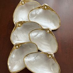 four white shells with pearls on them sitting on a wooden table next to each other