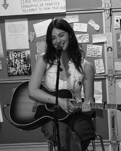 a woman sitting in front of a microphone while holding a guitar and singing into a microphone