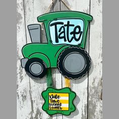 a green tractor shaped sign hanging on the side of a wooden fence that says tate