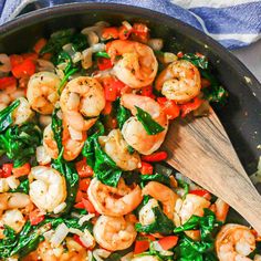 shrimp and spinach stir fry in a skillet with a wooden spoon on the side