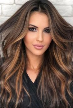 a woman with long, wavy hair is posing for the camera in front of a brick wall