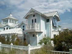 a blue house with white trim and balconies on the top floor is surrounded by tall grass