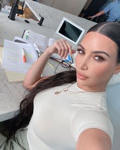 a woman sitting at a table with an open book and computer monitor in the background