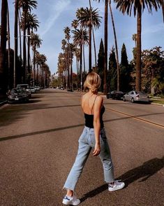 a woman is walking down the street with palm trees in the backgrouds