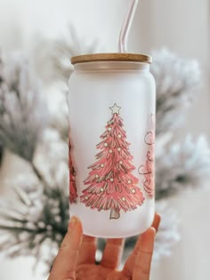 a hand holding a glass with a christmas tree painted on it and a straw in the cup