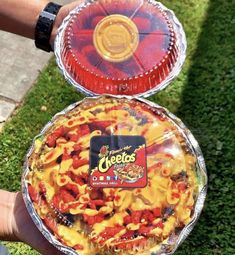 two pies that are sitting in the grass with one being held up by someone's hand