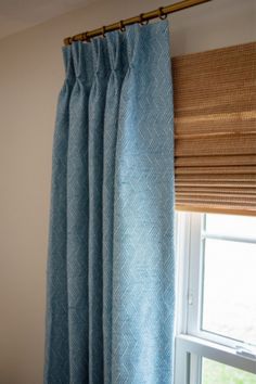 a window with blue curtains in front of it and a bamboo blind on the side