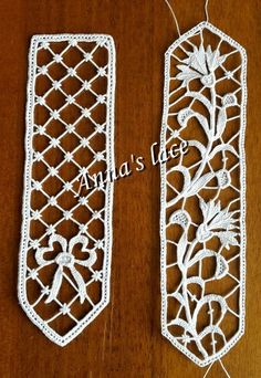 two white crocheted bookmarks with flowers on them sitting on top of a wooden table