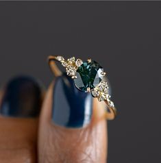 a woman's hand holding a ring with a green and white diamond on it