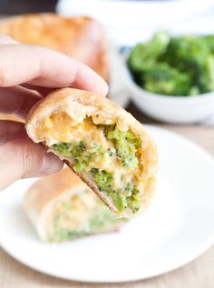 a hand holding a piece of broccoli and cheese pastry on a white plate