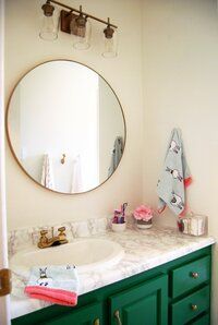 a bathroom with green cabinets and a round mirror