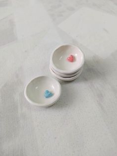 three small bowls with hearts on them sitting on a tableclothed surface, one is white and the other is blue