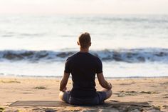 a man is sitting on the beach in front of the ocean and doing yoga exercises