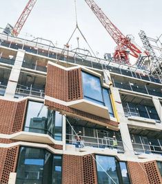 two cranes are on the side of a tall building with red bricks and glass windows