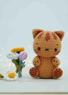 a crocheted teddy bear sitting next to a small vase with flowers in it