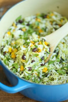 a blue bowl filled with rice, beans and veggies next to a wooden spoon