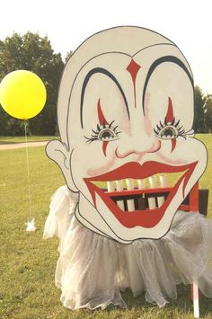 a creepy clown mask sitting on top of a wooden bench in the middle of a field