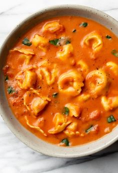 a bowl filled with pasta and sauce on top of a marble countertop next to a spoon