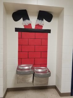 two silver trash cans sitting in front of a red brick wall with santa's hat on top