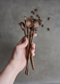 a person holding three wooden spoons with coffee beans scattered around them on a table