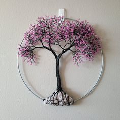 a wire tree with pink flowers on it hanging from a wall above a round metal frame