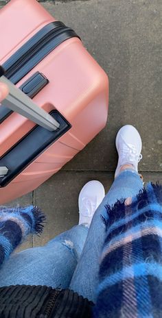 a person standing next to a pink piece of luggage on the ground with their feet up