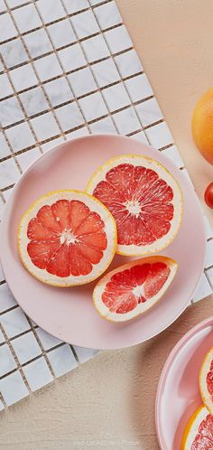 grapefruits cut in half on pink plates next to tomatoes and oranges