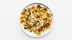 a white plate topped with pasta covered in sauce and nuts on top of a table