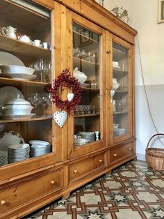 a wooden china cabinet filled with dishes and glasses on top of a tiled floor next to a basket