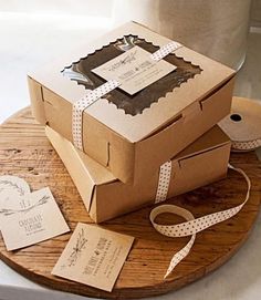 two brown boxes with white ribbons and tags on a wooden tray next to a roll of toilet paper