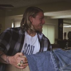 a man with long hair wearing a white t - shirt and blue jeans is holding onto another person's leg