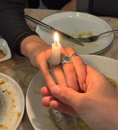 a person holding a lit candle in their hand at a table with food and utensils