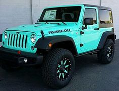 a blue jeep is parked in front of a building with black tires and rims