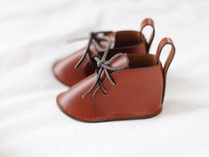 A symbol of enduring love and tenderness, these hand crafted leather baby shoes are designed to be cherished for generations. Classic lace up design, complete with leather laces and soles. Entirely made by hand, using traditional leather crafting methods for superior craftsmanship, attention to detail, and durability. Saddle stitched with wax linen thread. Hand painted edges with edge paint from France. Italian vegetable tanned leather is supple with good structure and a soft sheen. It will pati