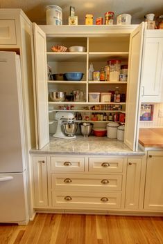 an organized kitchen with white cabinets and wood flooring is pictured in this image, there are many items on the shelves