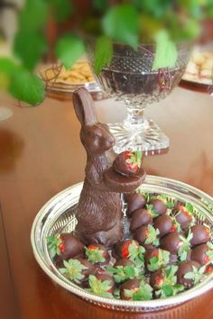 chocolate bunny sitting on top of strawberries in front of a glass bowl filled with flowers