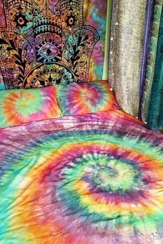 a bed covered in colorful tie - dyed comforter and pillow cases next to a window