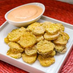 a white plate topped with fried food next to a bowl of dipping sauce on a red place mat