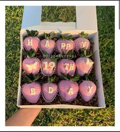 a box filled with chocolate covered strawberries sitting on top of grass next to a person's hand